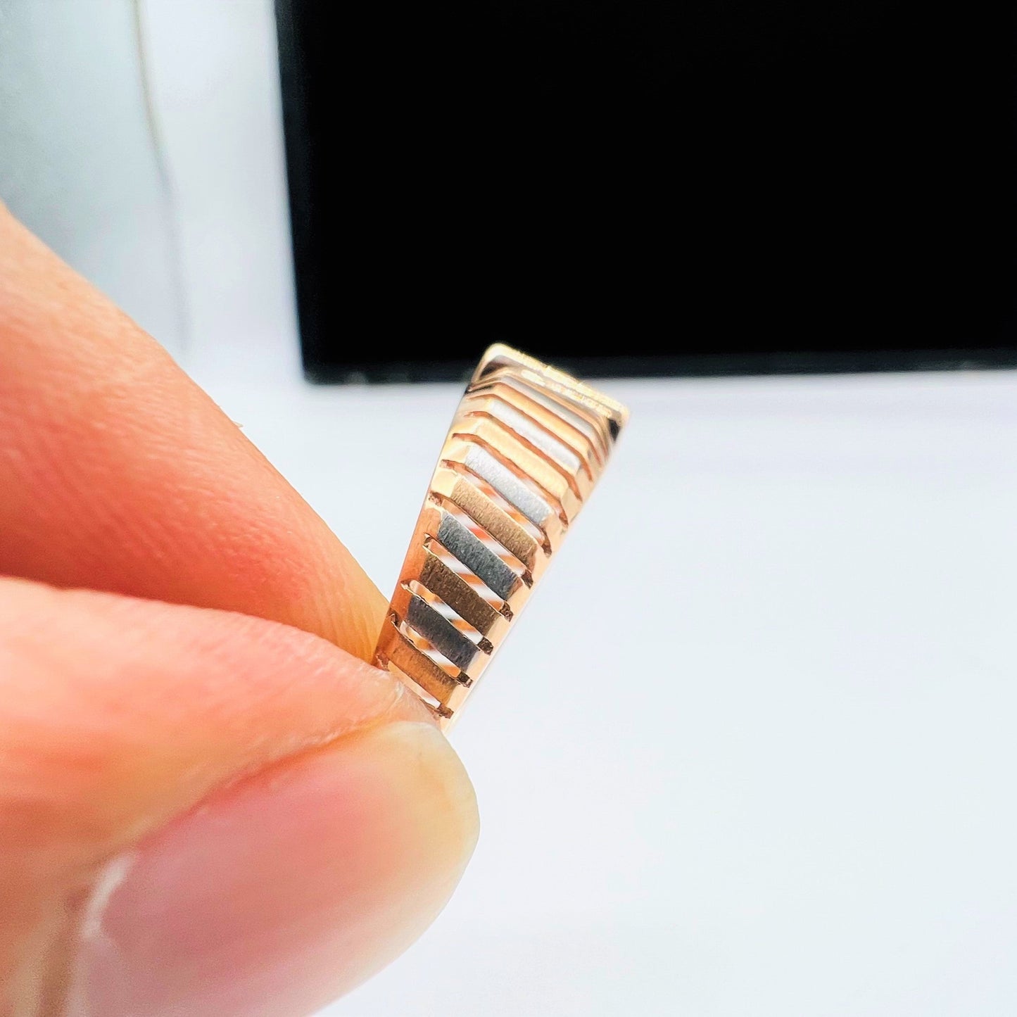 A man's hand displaying a gold diamond ring with round cut diamonds set in a square shape from the side.