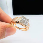 A man's hand displaying a gold diamond ring with round cut diamonds set in a square shape.