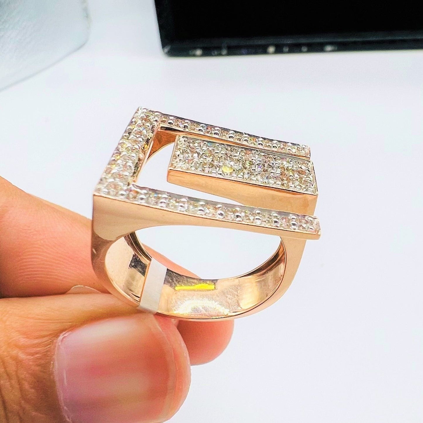 A man's hand displaying a gold diamond ring with a large square shape with round cut diamonds on top.