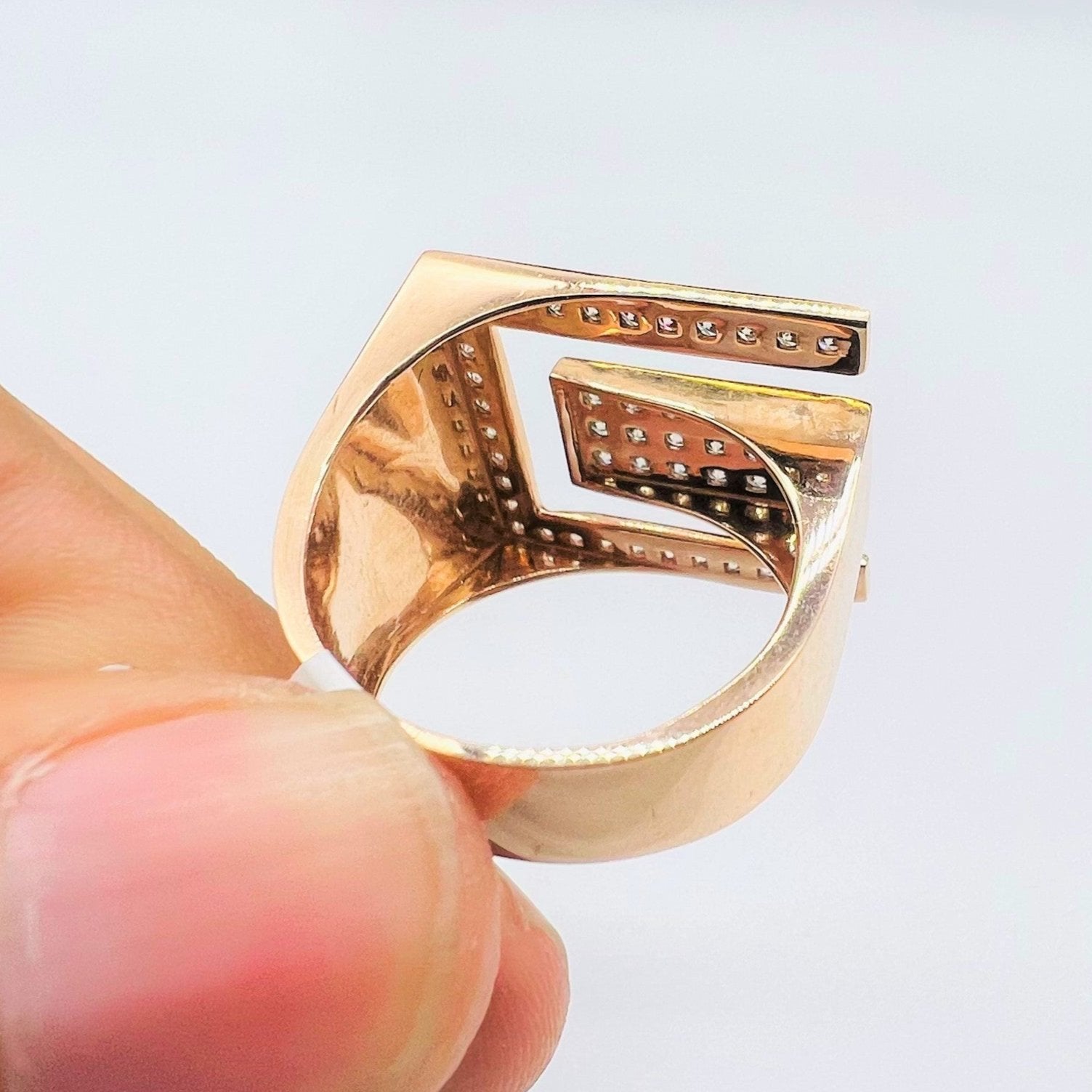 A man's hand displaying a gold diamond ring with a large square shape with round cut diamonds on top.