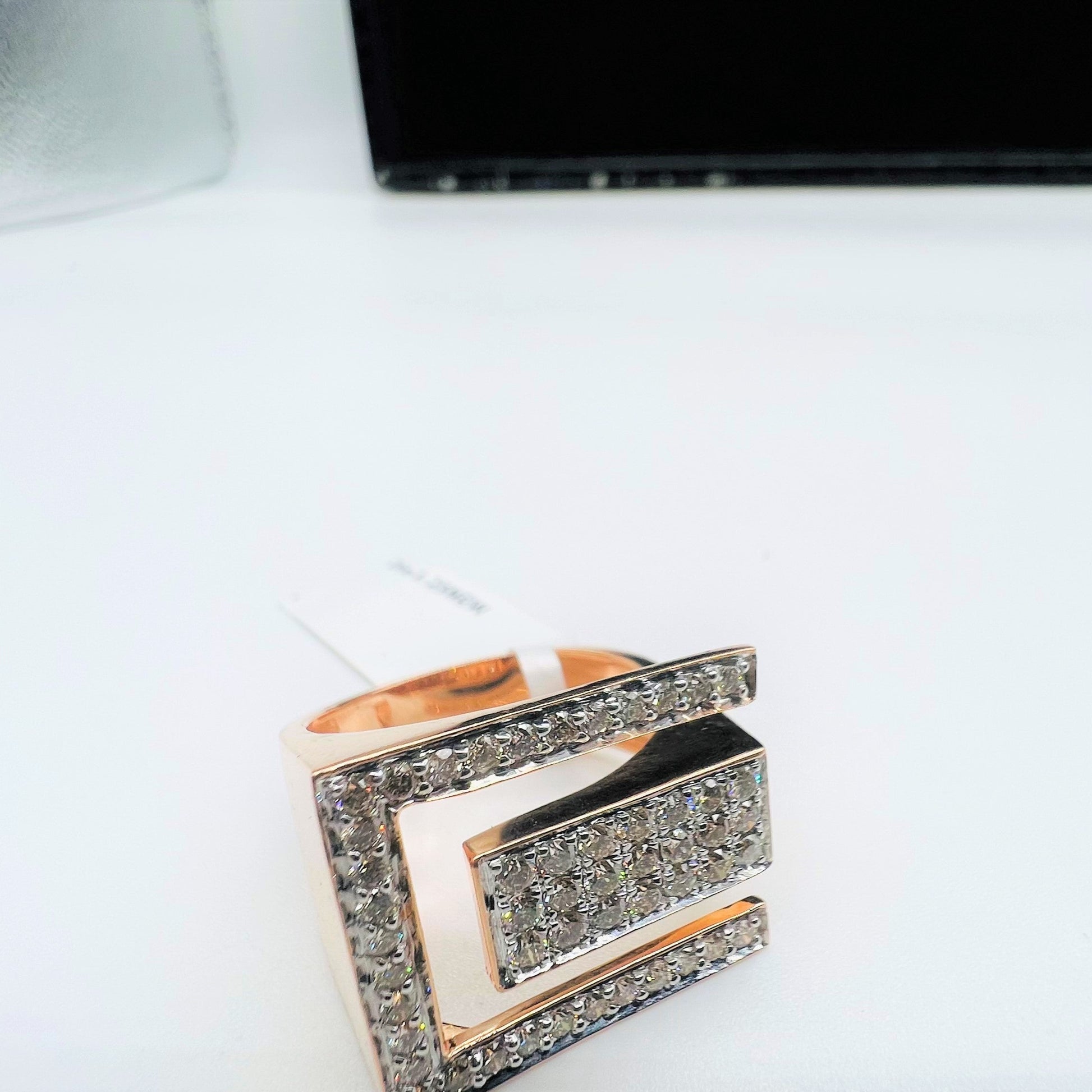 A gold diamond ring with a large square shape with round cut diamonds on top displayed on a white surface.