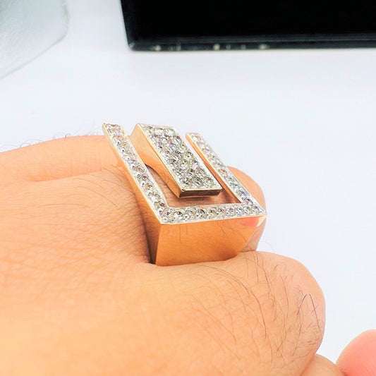 A man's hand displaying a gold diamond ring with a large square shape with round cut diamonds on top.