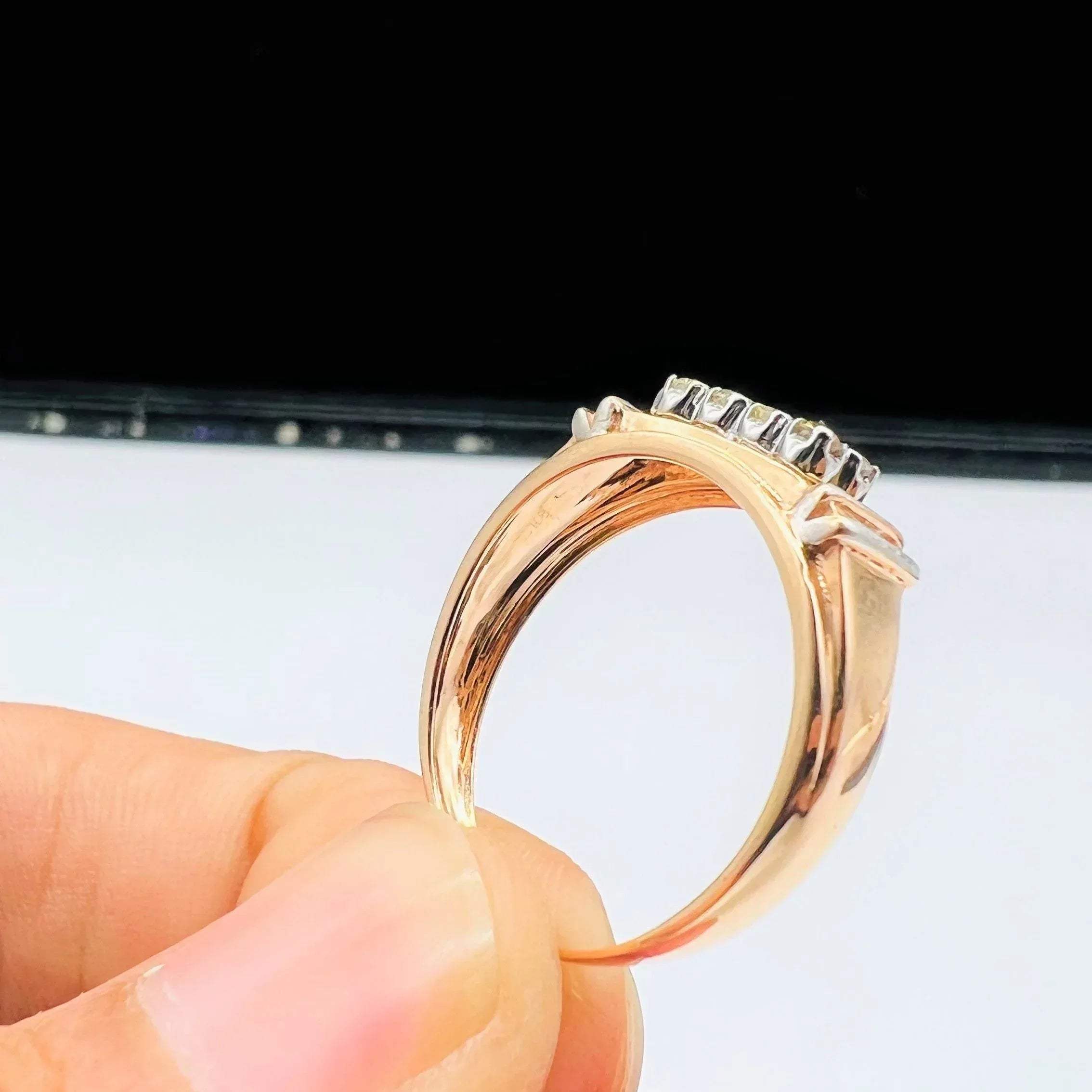 A man's hand displaying a gold diamond ring with round cut diamonds.