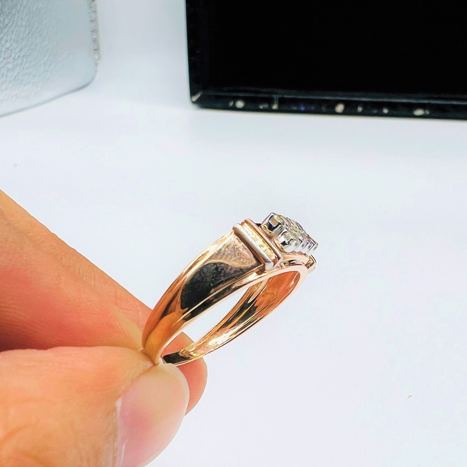 A man's hand displaying a gold diamond ring with round cut diamonds.