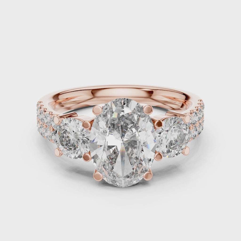 Rose gold ring with a large oval shape diamond in center, 2 round shape diamonds a little bit smaller than center diamond studded on both side of center diamond and some small round diamonds studded after that, is rotating on a white surface.