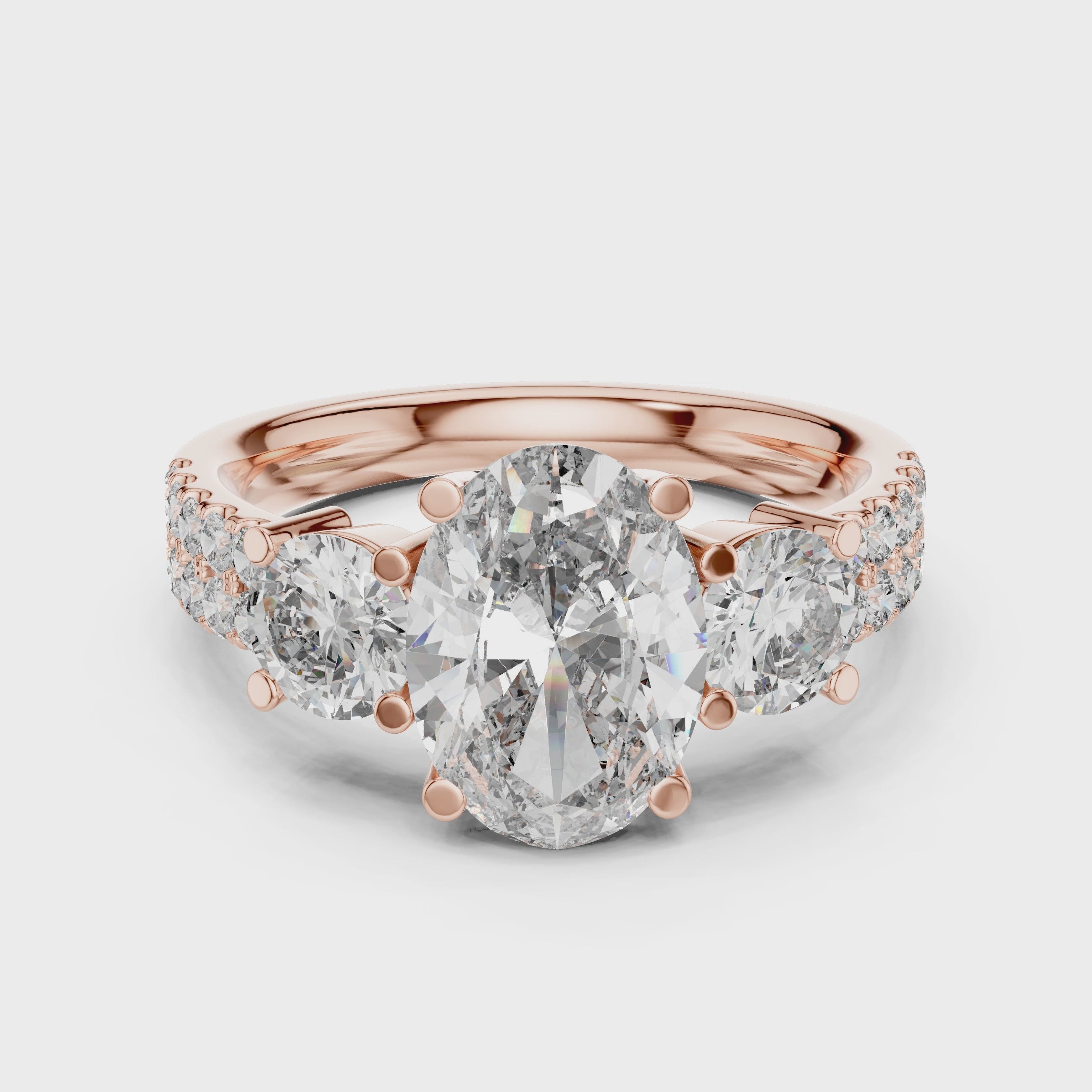 Rose gold ring with a large oval shape diamond in center, 2 round shape diamonds a little bit smaller than center diamond studded on both side of center diamond and some small round diamonds studded after that, is rotating on a white surface.