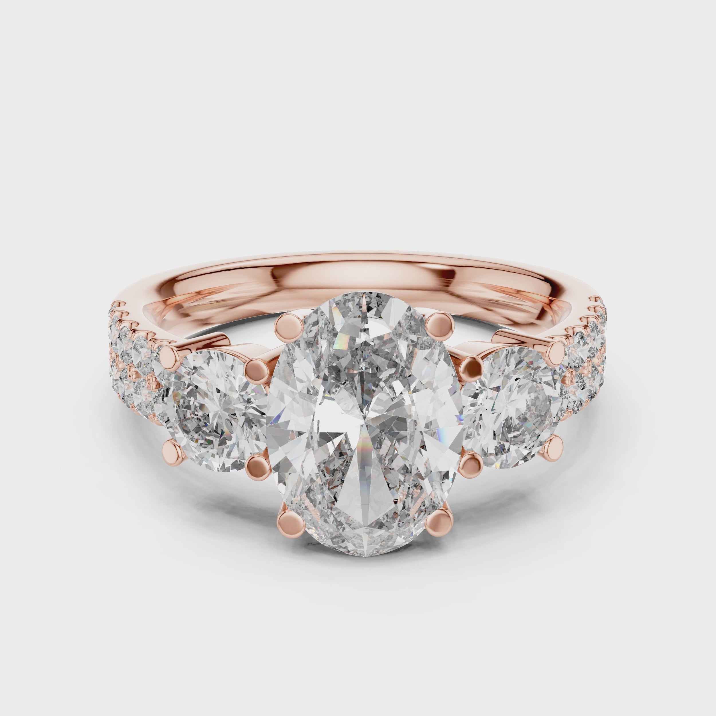 Rose gold ring with a large oval shape diamond in center, 2 round shape diamonds a little bit smaller than center diamond studded on both side of center diamond and some small round diamonds studded after that, is rotating on a white surface.