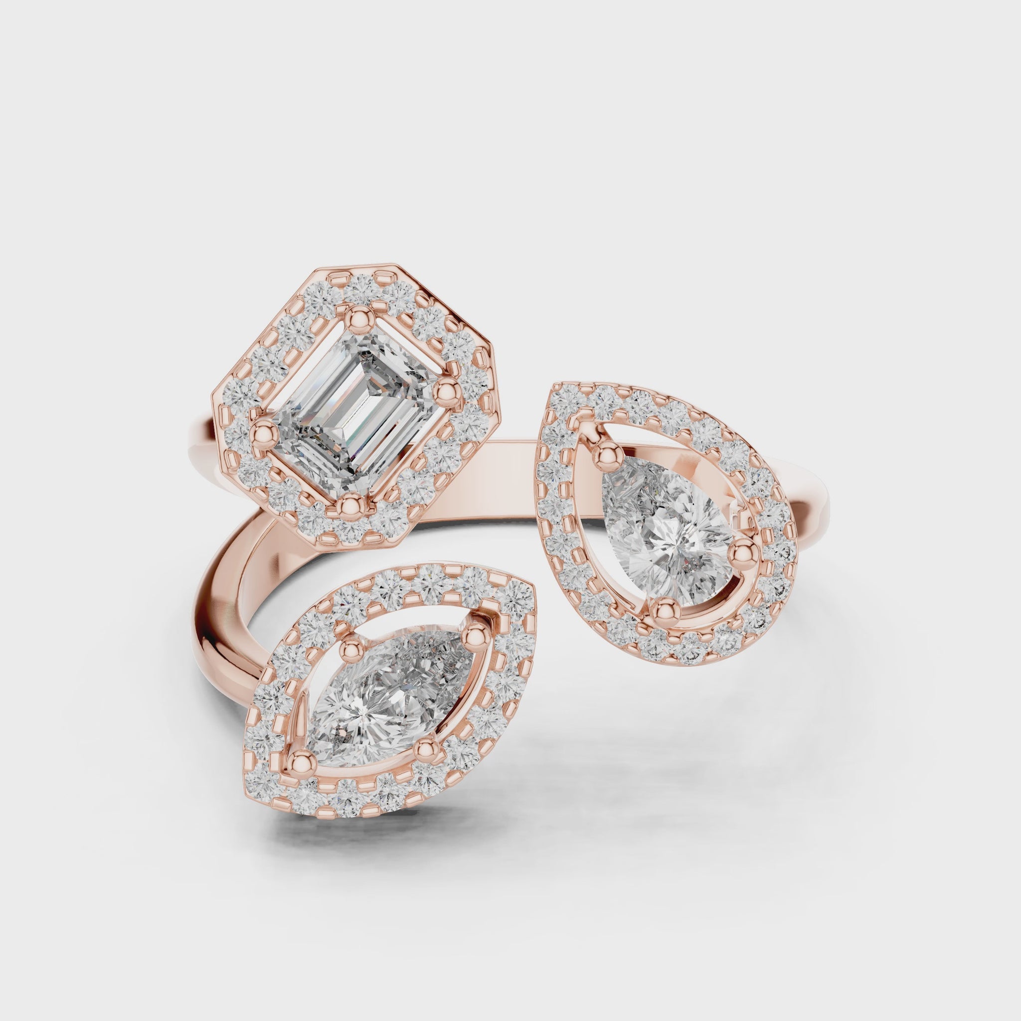 A gold ring that contains 1 pear, 1 marquise and 1 emerald shaped diamonds and halo of diamonds around these three diamonds, showing from 360 degree angle.