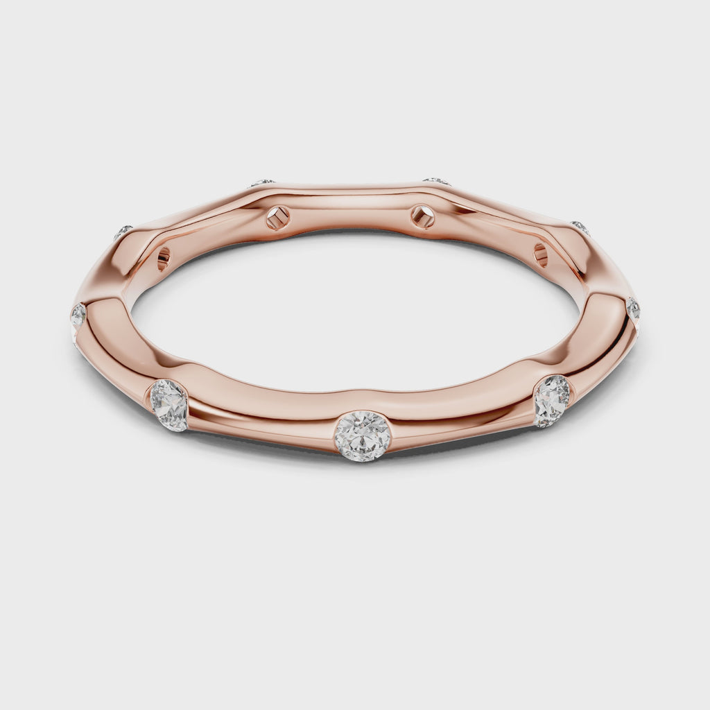 Rose gold ring with diamond accents is rotating horizontally on a white surface.
