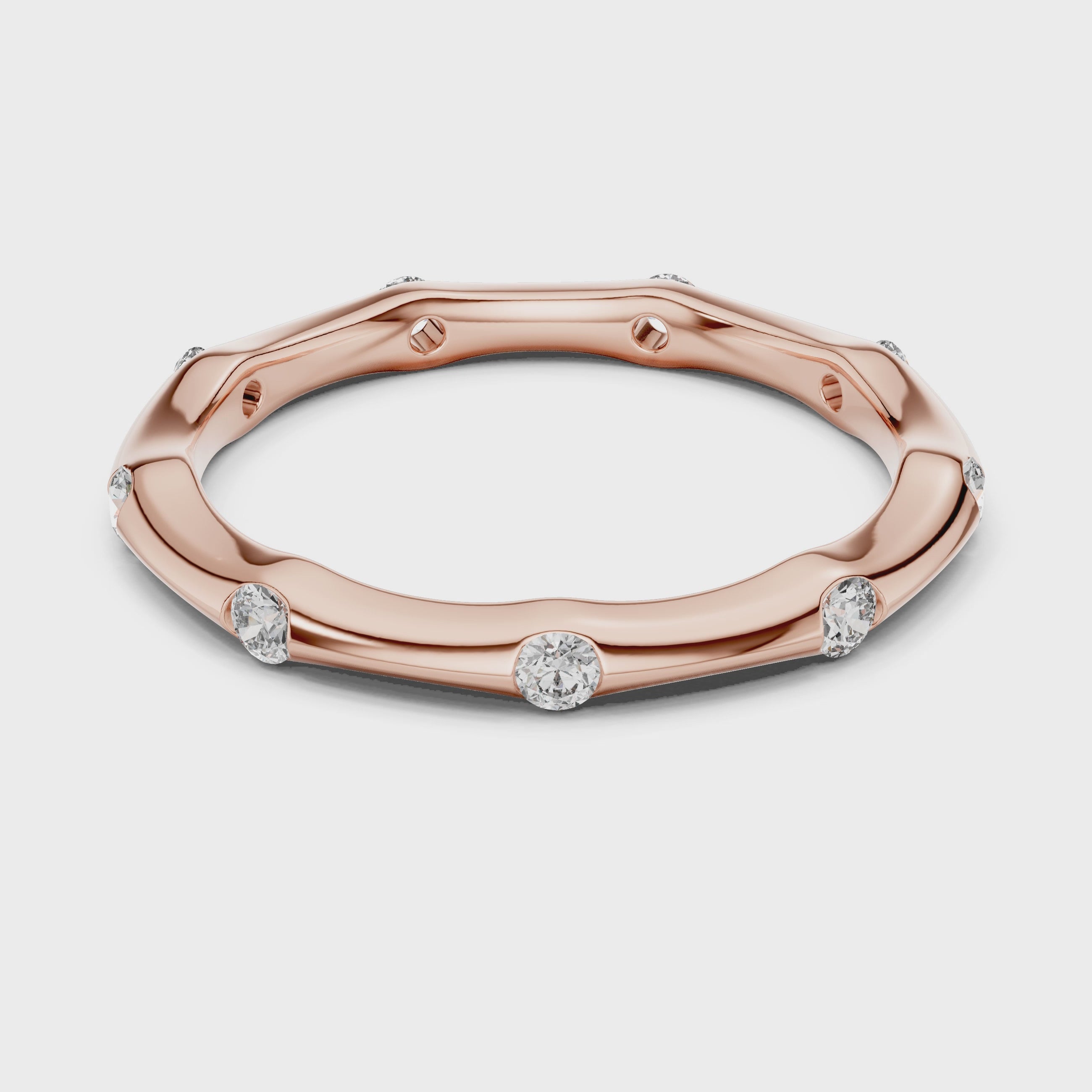 Rose gold ring with diamond accents is rotating horizontally on a white surface.