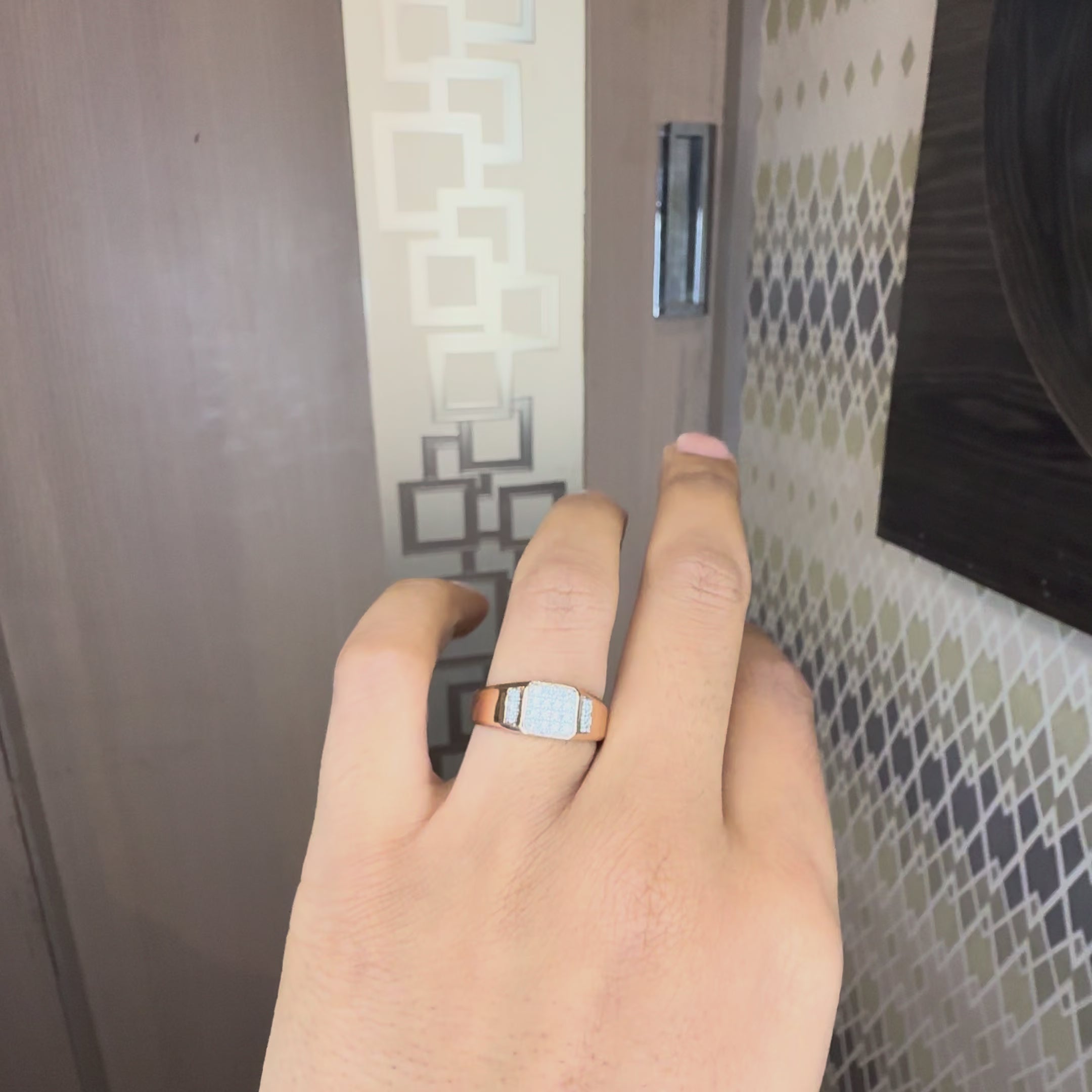 A gold ring with a square pavé diamond center and a small side channel of diamonds, displayed worn in a hand's finger and the hand is tilting both sides to show the ring from every angle.