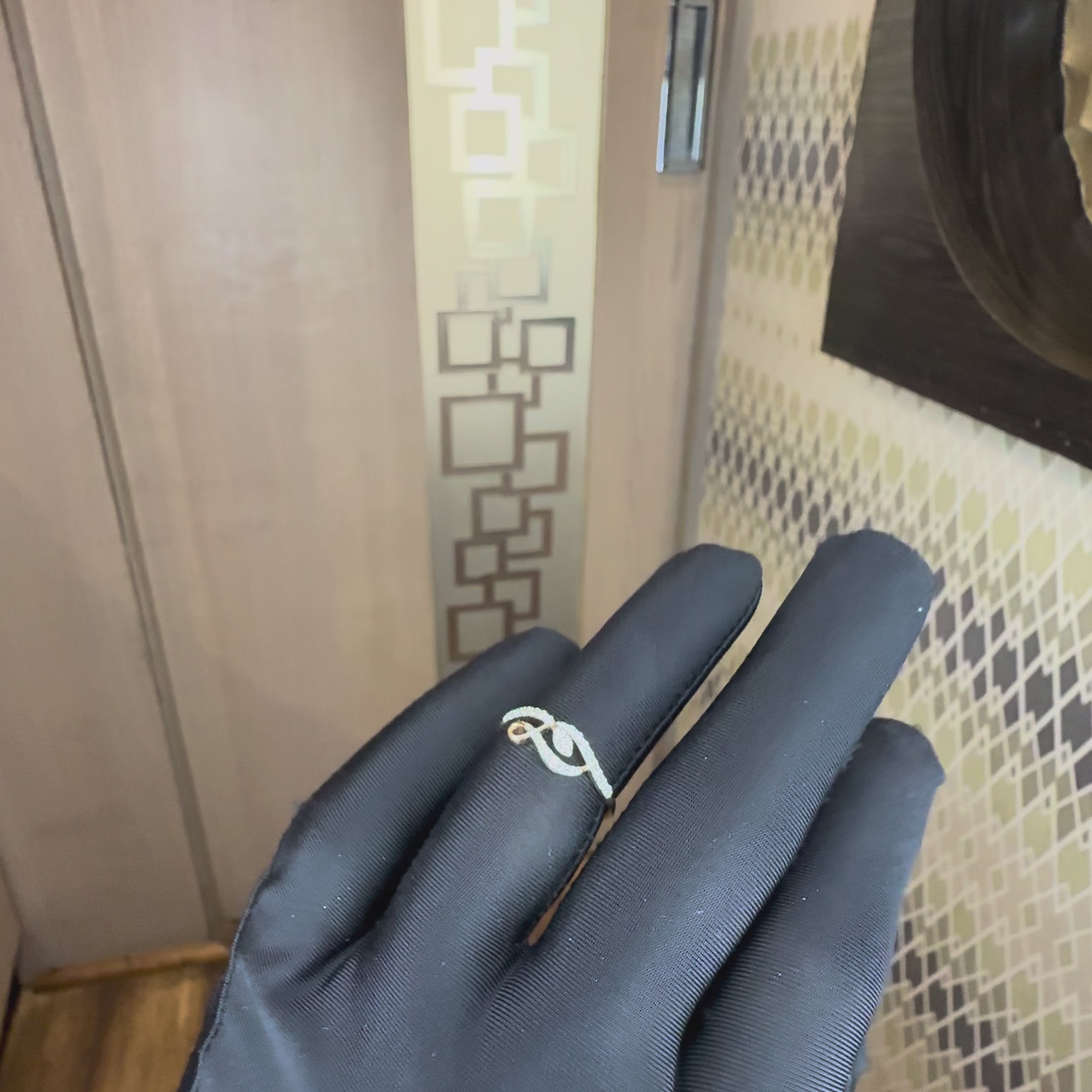 A rose gold ring with a curved, openwork design paved with small clear stones, shown on a black gloves worn hand against a neutral background.