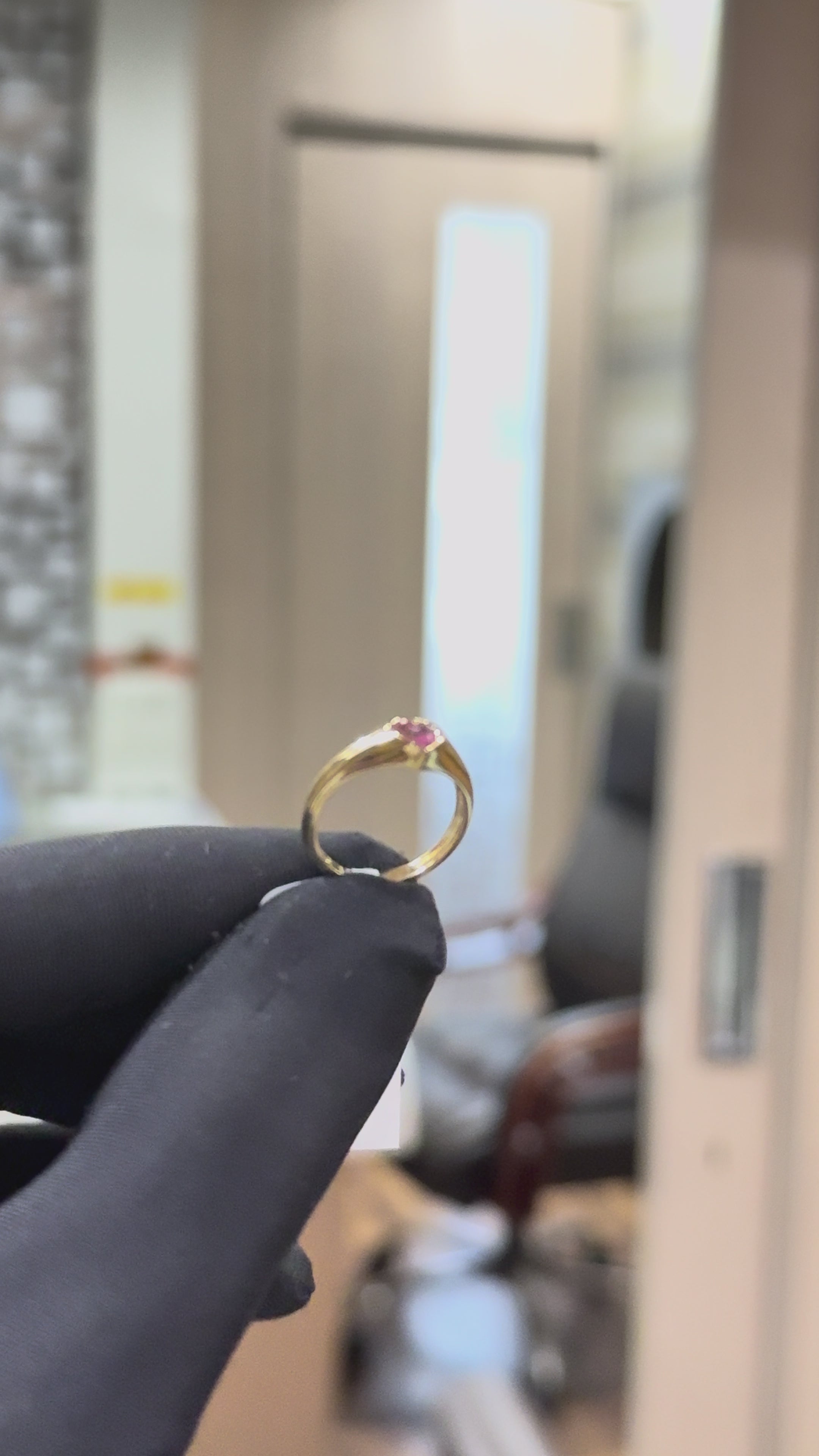 a men's hand is showing gold ring with a heart-shaped pink sapphire gemstone against a natural background.