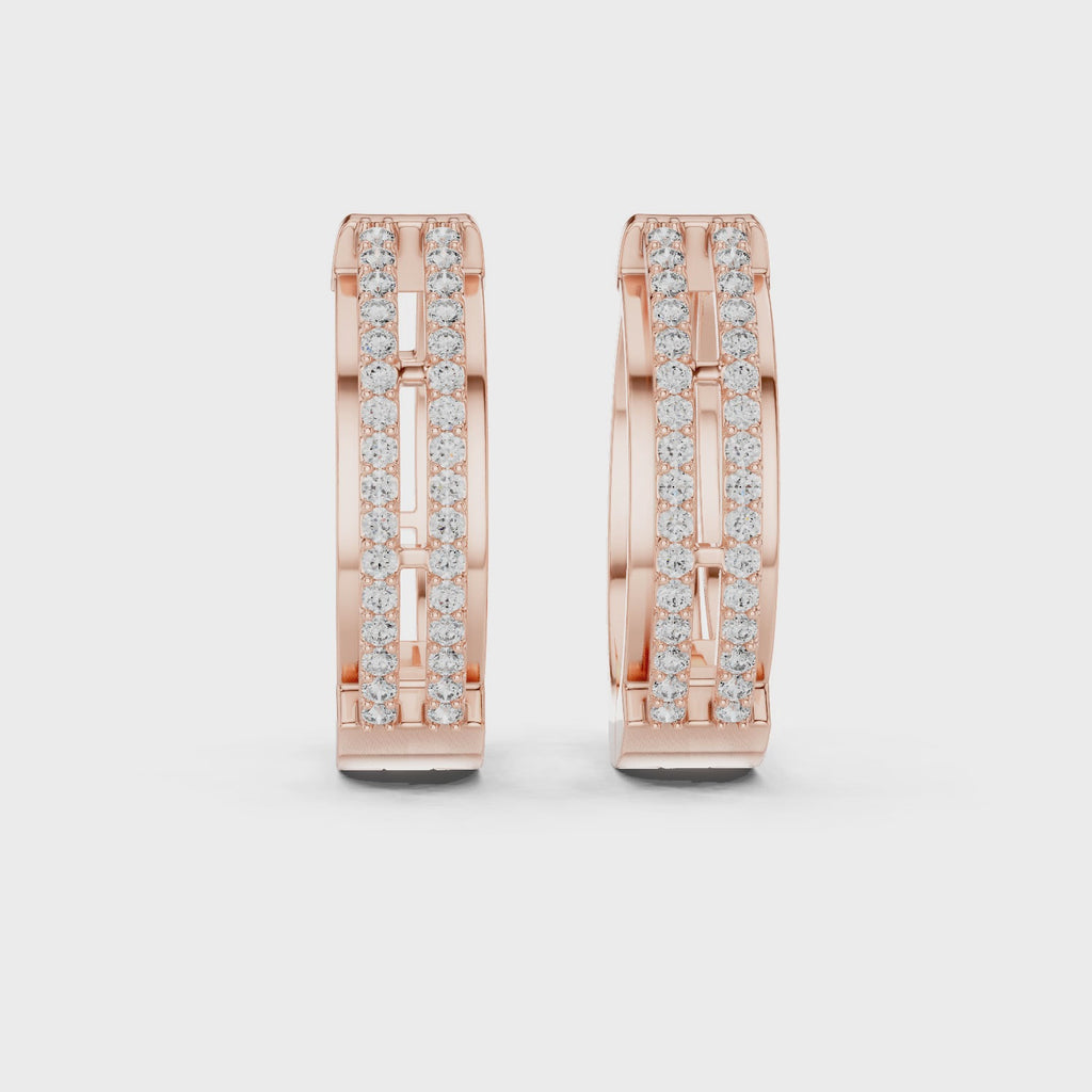 Rose gold huggie hoop earrings with two diamond rails are rotating horizontally on a white surface.