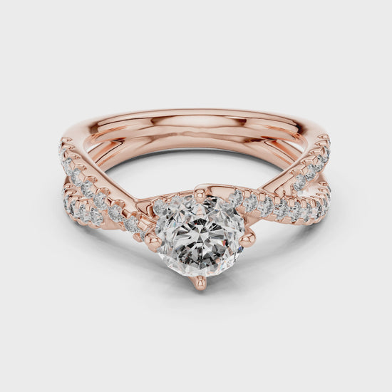 A rose gold ring with diamonds is rotating horizontally on a white surface. The ring has 1 large diamond in the center and other small diamonds are studded on a shank.