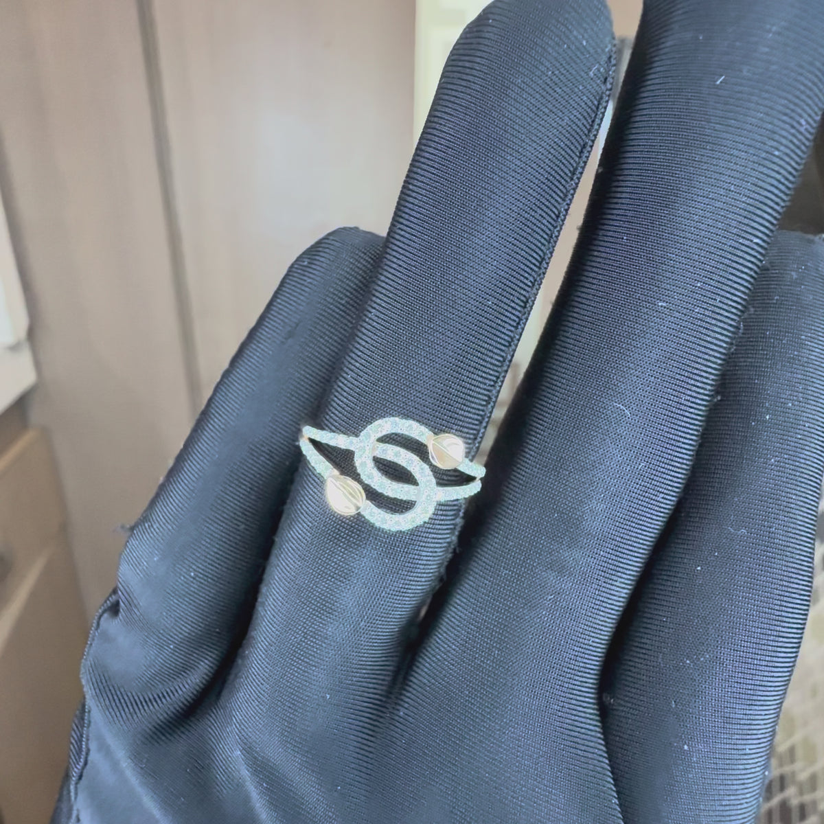 A delicate ring with intertwined gold bands, accented by small pavé-set clear stones and two gold leaf shaped details, shown by a black gloves hand from the close.