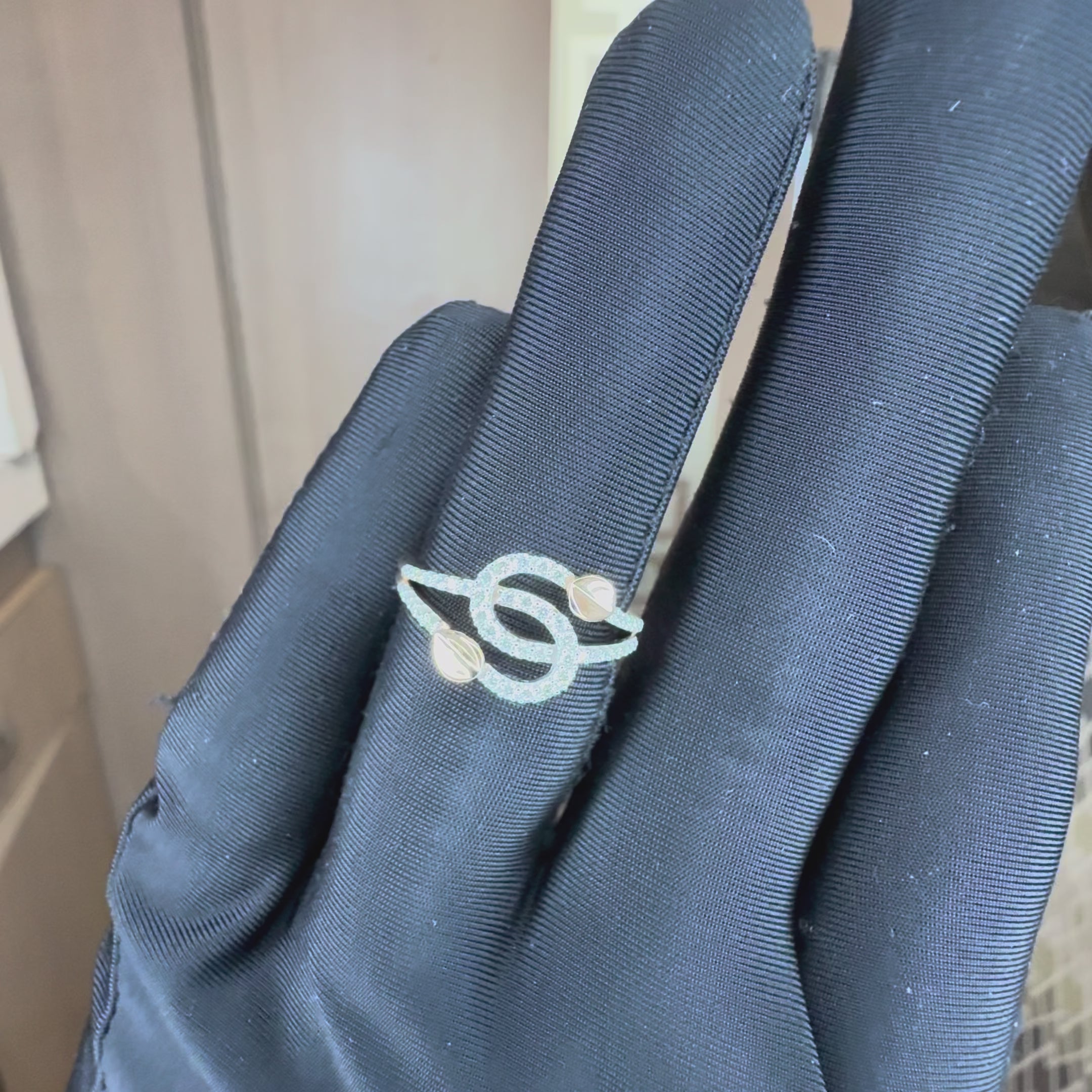 A delicate ring with intertwined gold bands, accented by small pavé-set clear stones and two gold leaf shaped details, shown by a black gloves hand from the close.
