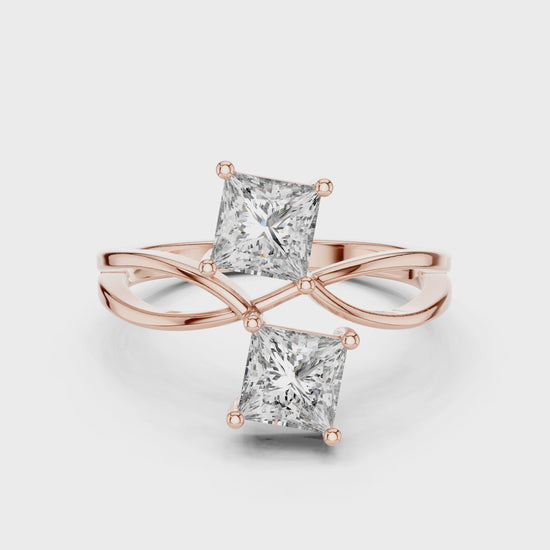 Rose gold ring with two princess-cut diamonds on a white background showing from the 360 degree angle.