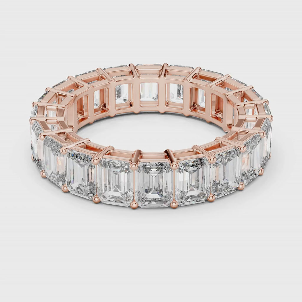 Rose gold ring with emerald-cut natural diamonds on a white surface is rotating all around.
