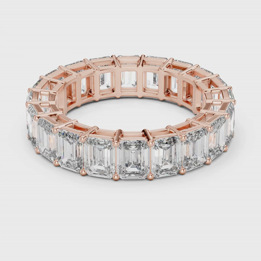 Rose gold ring with emerald-cut natural diamonds on a white surface is rotating all around.