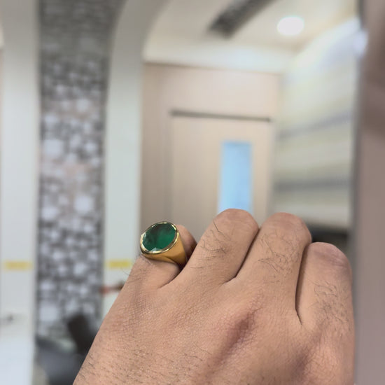 Gold ring with a green emerald stone on shown by a hand