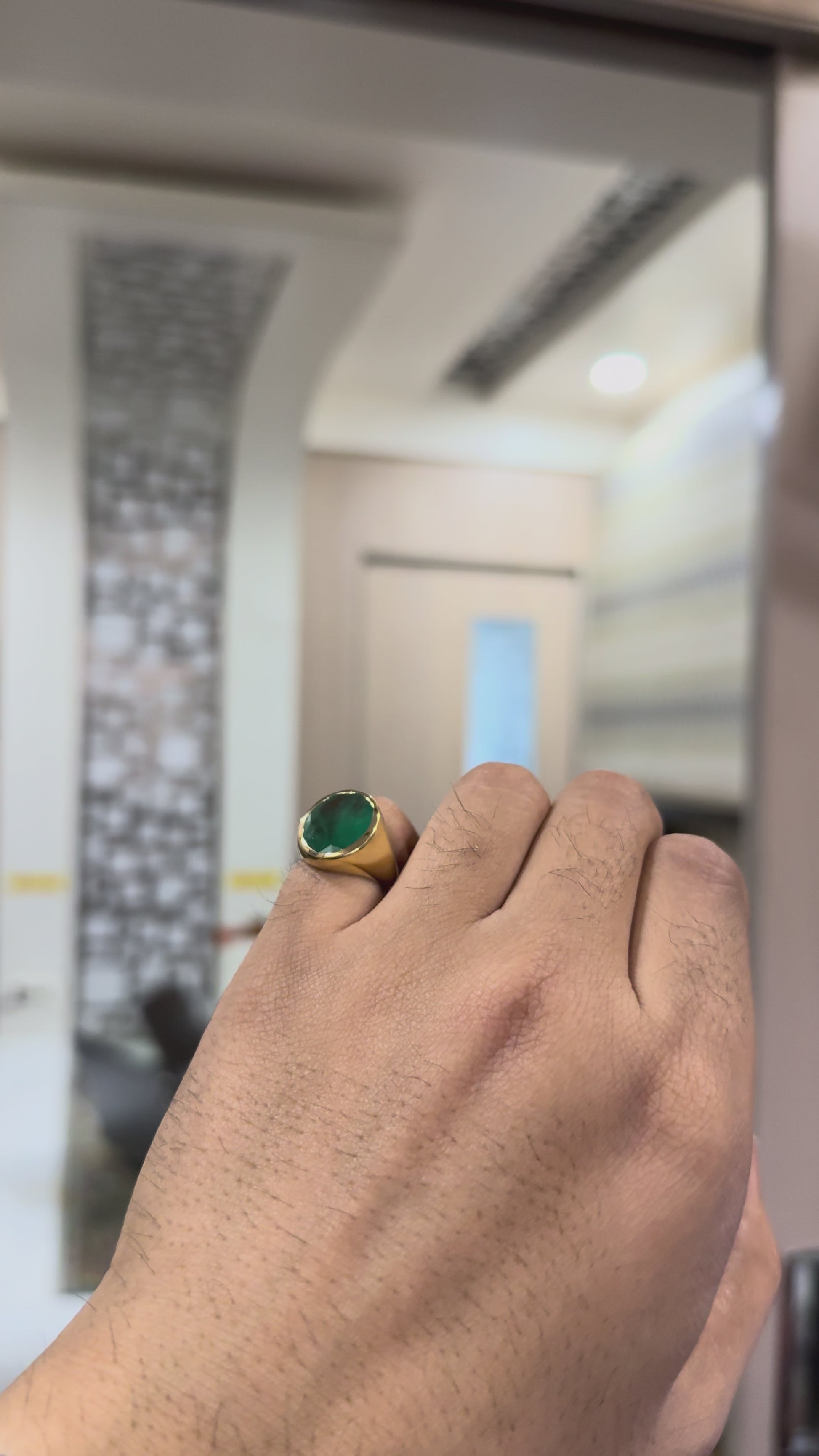 Gold ring with a green emerald stone on shown by a hand