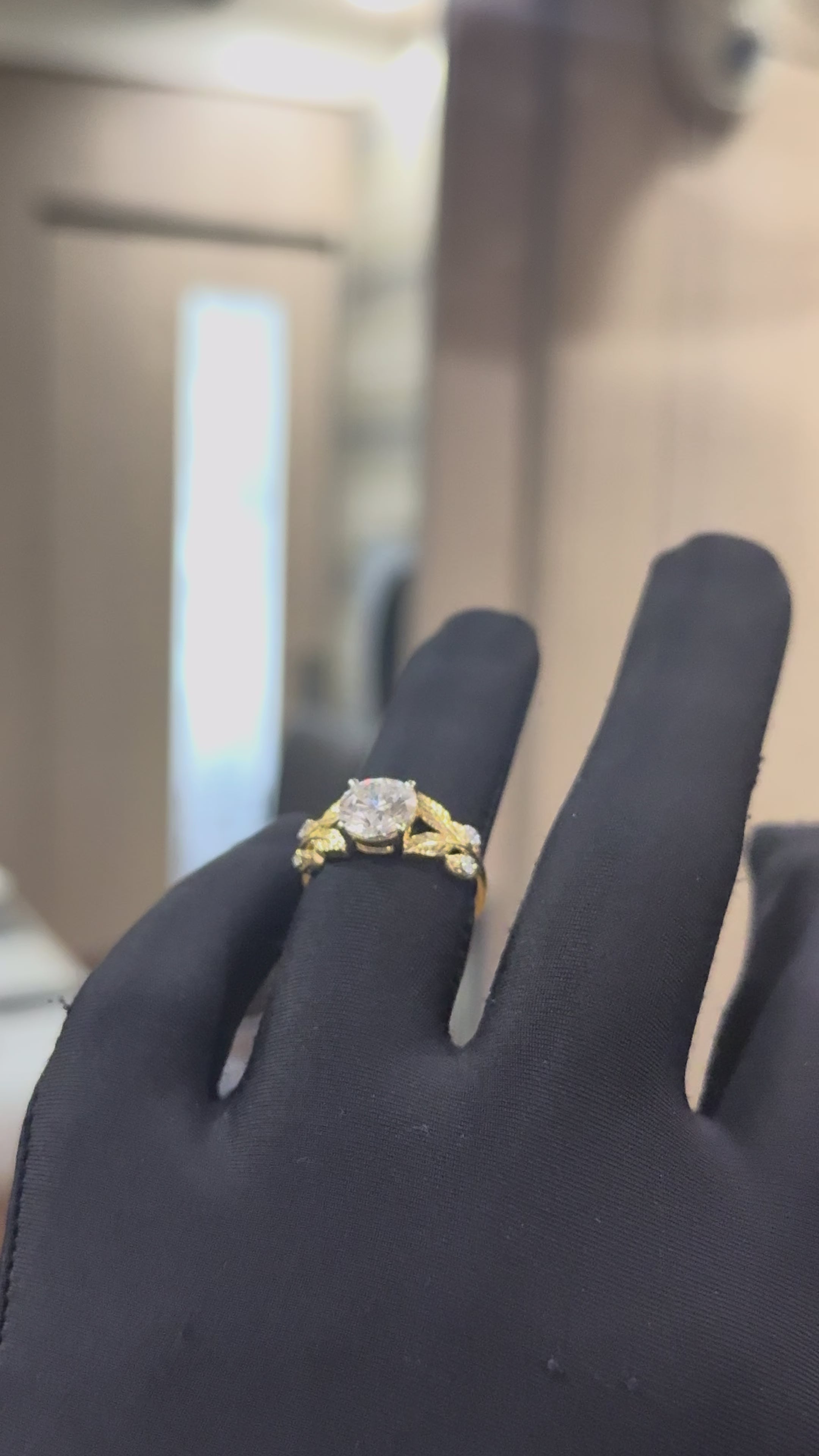 Gold ring with diamond and leaf designs against a natural background shown by a hand.