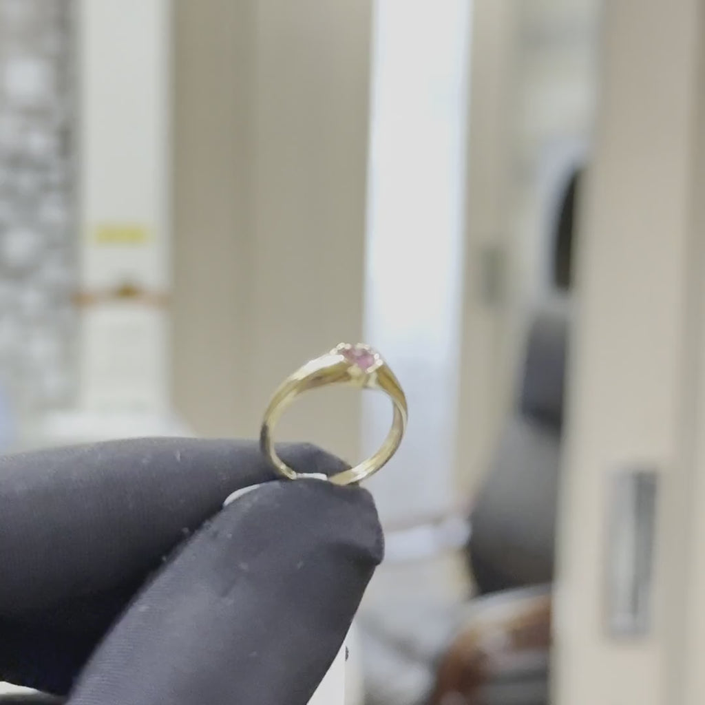 a men's hand is showing gold ring with a heart-shaped pink sapphire gemstone against a natural background.