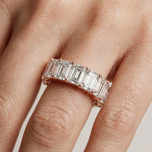 Rose gold ring with emerald-cut natural diamonds on a hand against a neutral background