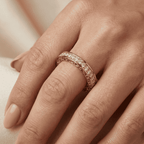 Rose gold ring with natural diamonds on a hand against a neutral background