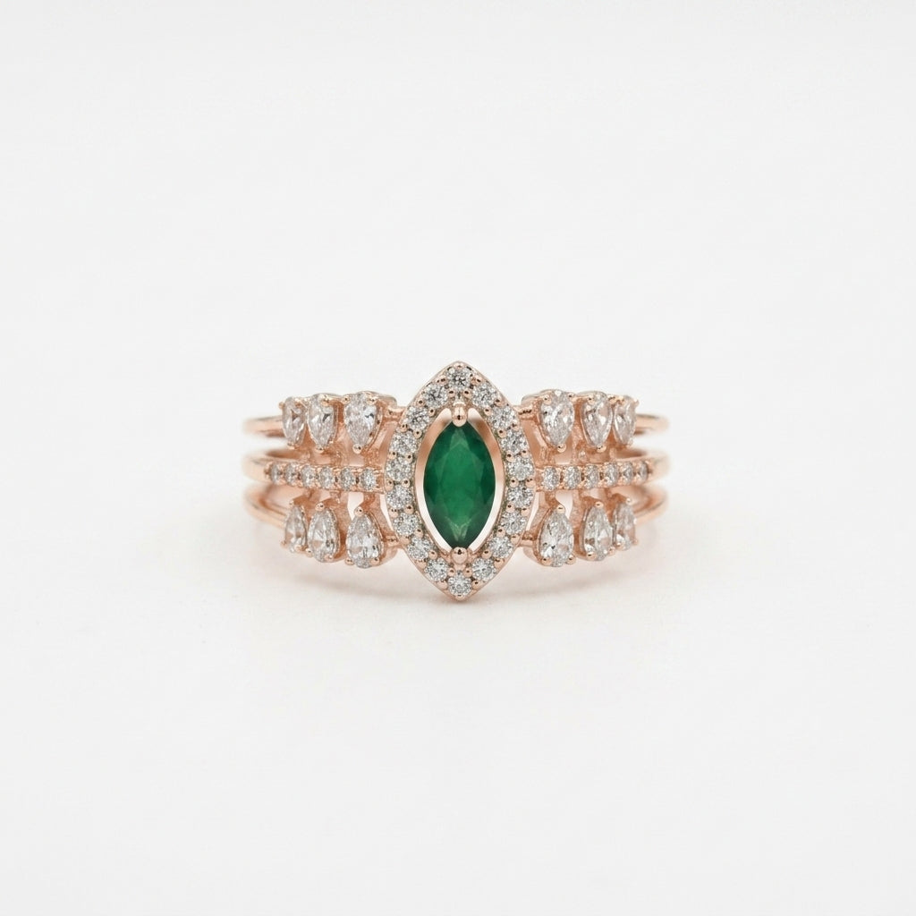 A rose gold ring featuring a central marquise-cut green emerald surrounded by a halo of small clear stones, with additional clear stones along the band, set against a plain white background.