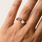 A close-up of a hand wearing a rose gold ring with two square frames where diamonds are studded in pave setting, set against a plain light background.