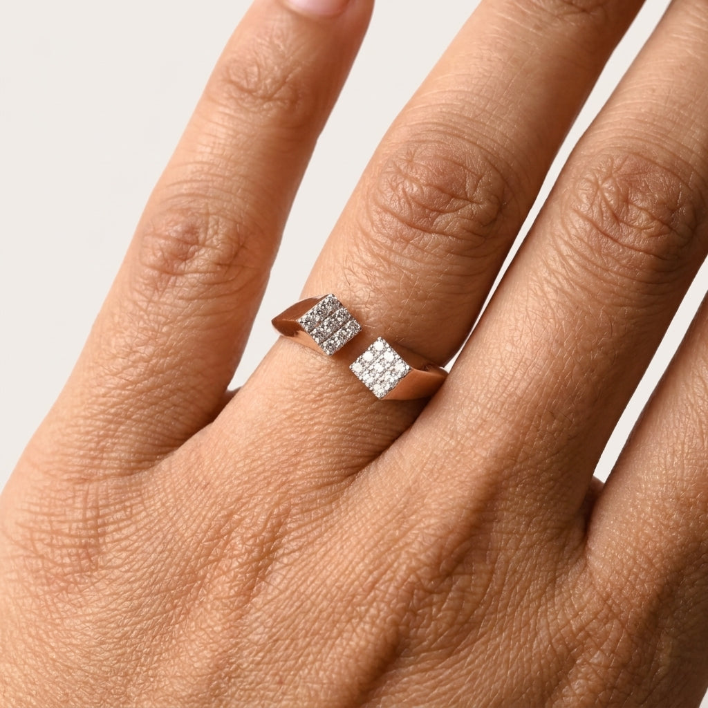 A close-up of a hand wearing a rose gold ring with two square frames where diamonds are studded in pave setting, set against a plain light background.