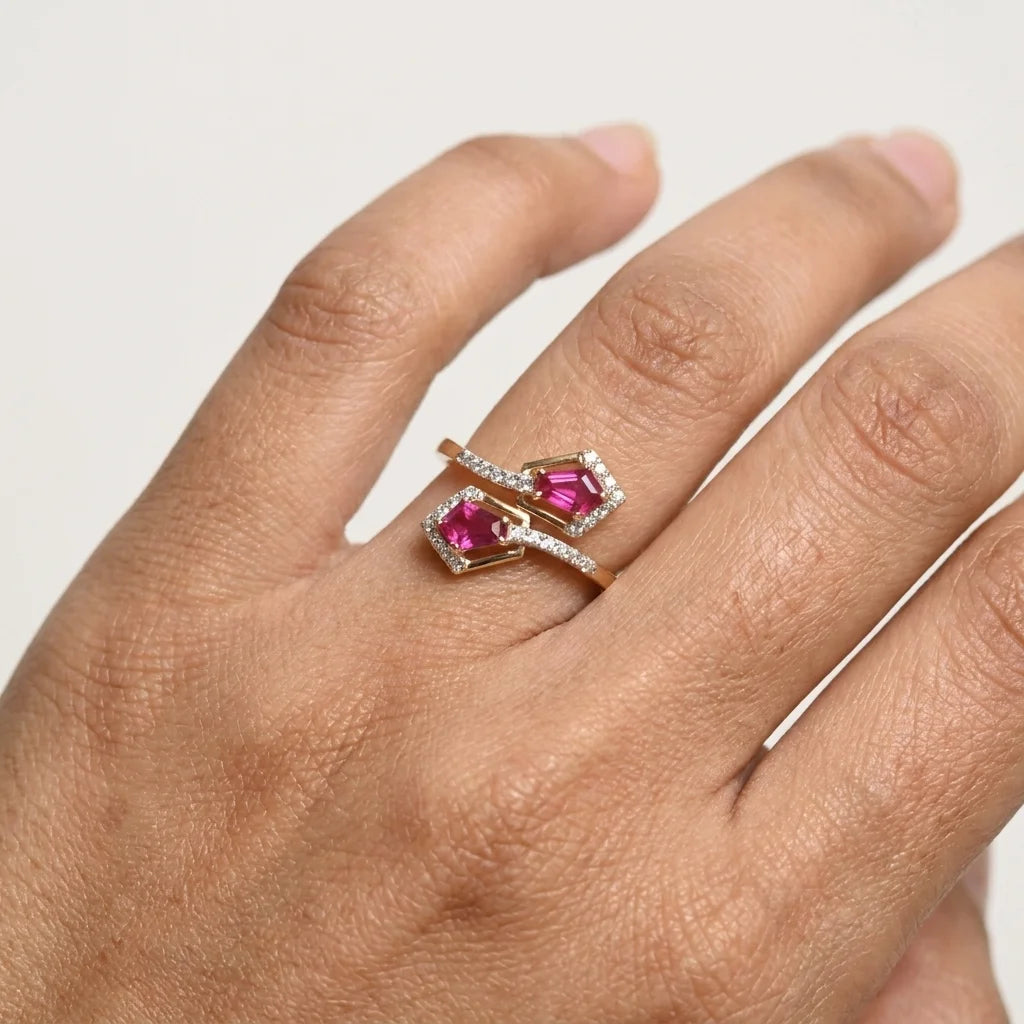 A close-up lifestyle shot of a person wearing a gold ring with a clear pavé diamond halo around the pink gemstones center on his ring finger, against a white background.