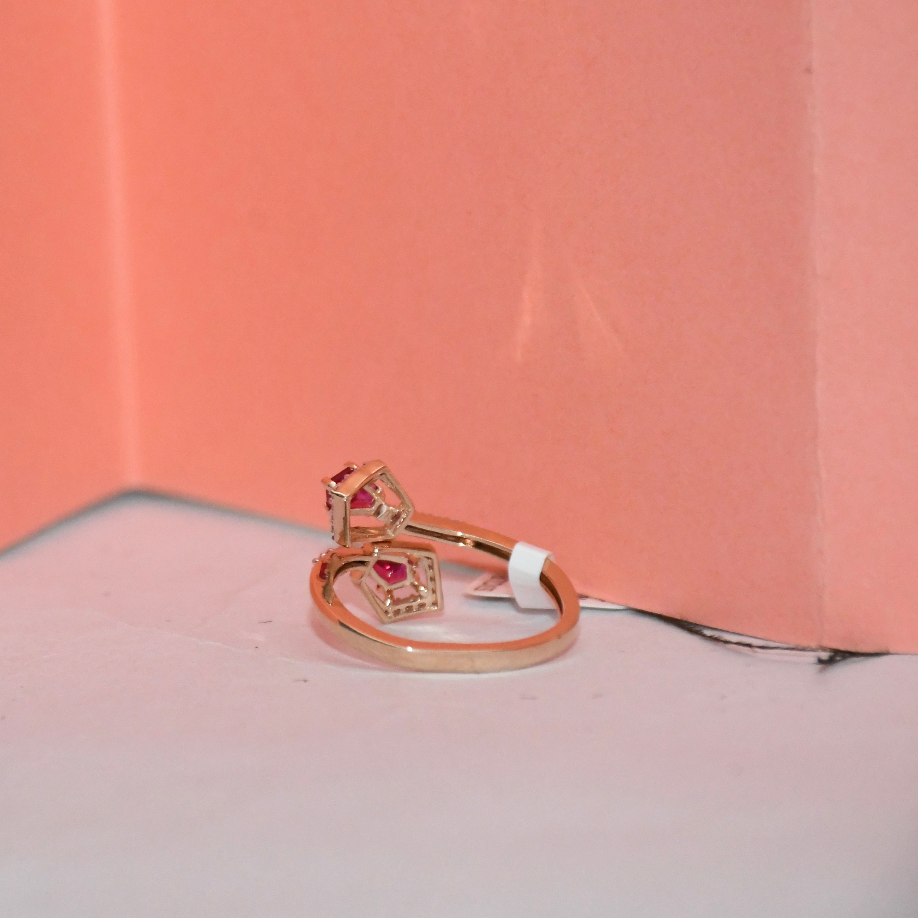 A rose gold ring with a pavé setting and small pink gemstones, resting on a white surface against a peach-pink background.