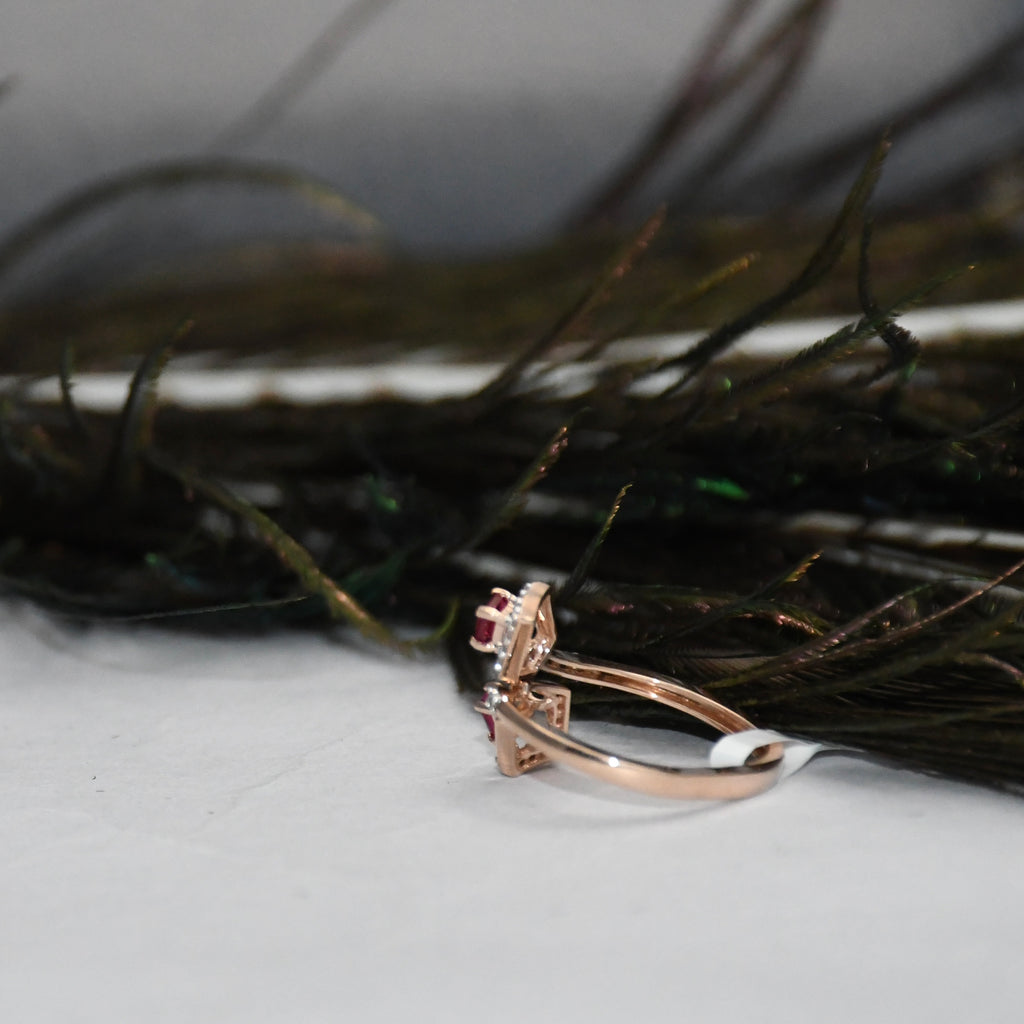 A rose gold ring with a small clear gemstone cluster, resting on a white surface in front of dark feathers.