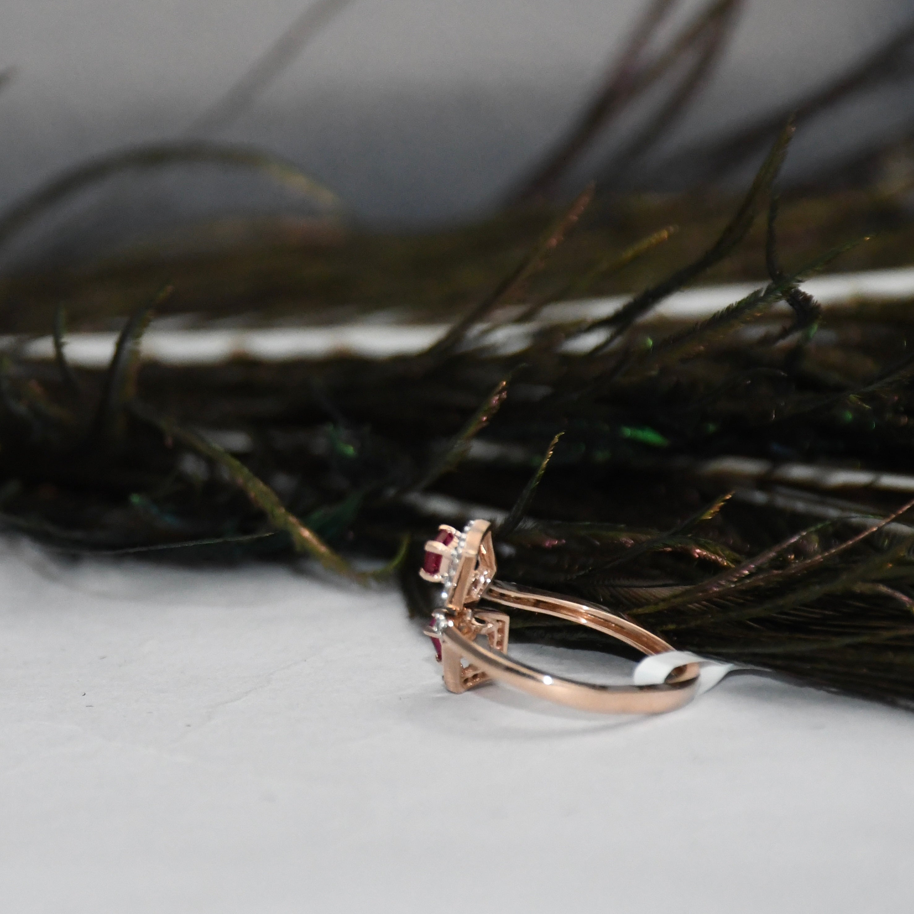 A rose gold ring with a small clear gemstone cluster, resting on a white surface in front of dark feathers.