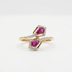 A gold ring with two diamond-paved halos surrounding pink gemstones, displayed on a clean white background.