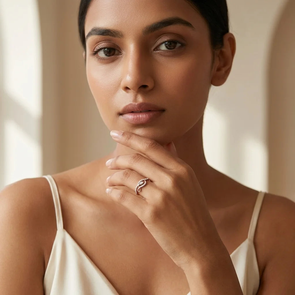 A close-up lifestyle shot of a woman wearing a delicate gold ring with small diamonds on her finger, set against a soft beige background.
