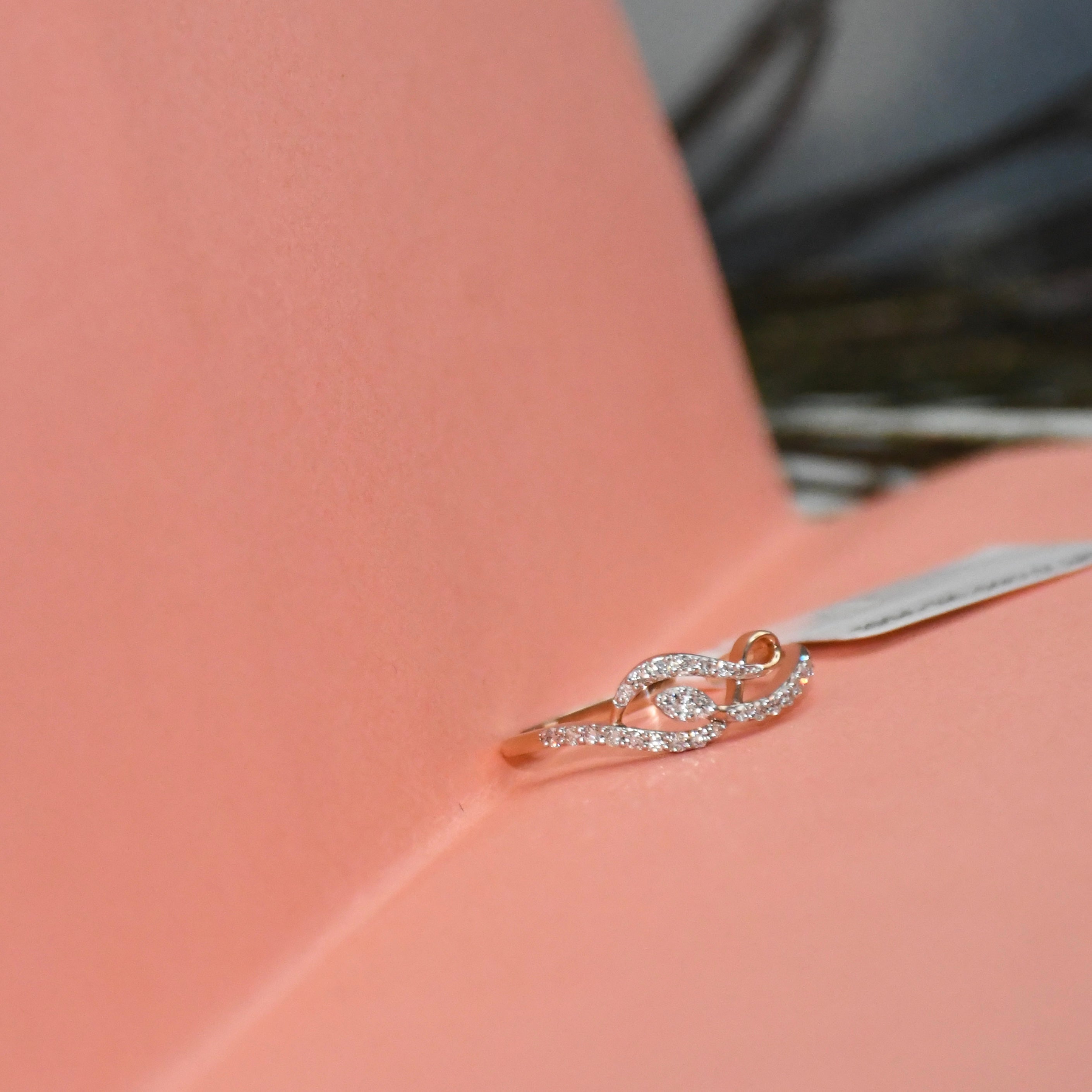 A delicate rose gold ring with pavé-set clear stones, resting on a textured pink surface.