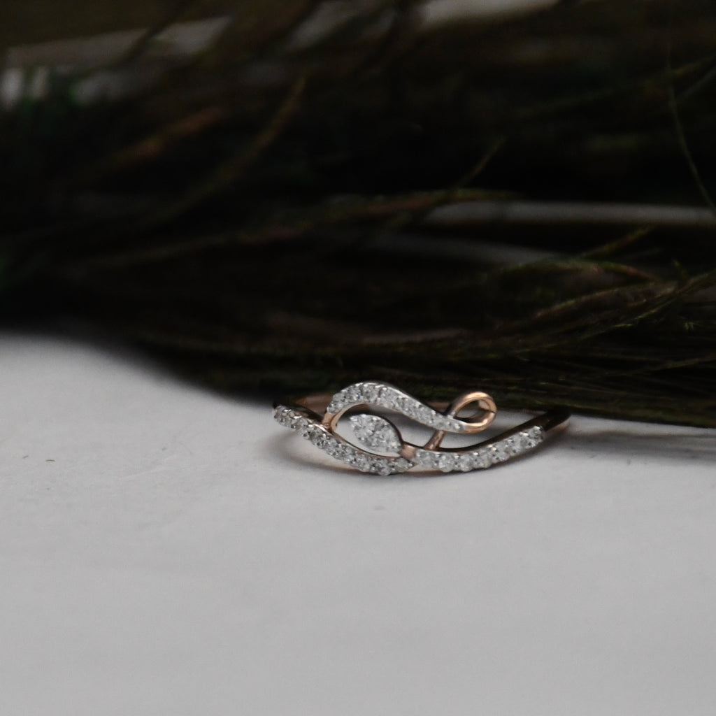 A delicate ring with a curved, leaf-like design paved with clear stones, featuring rose gold accents on a white surface with dark feathers in the background.