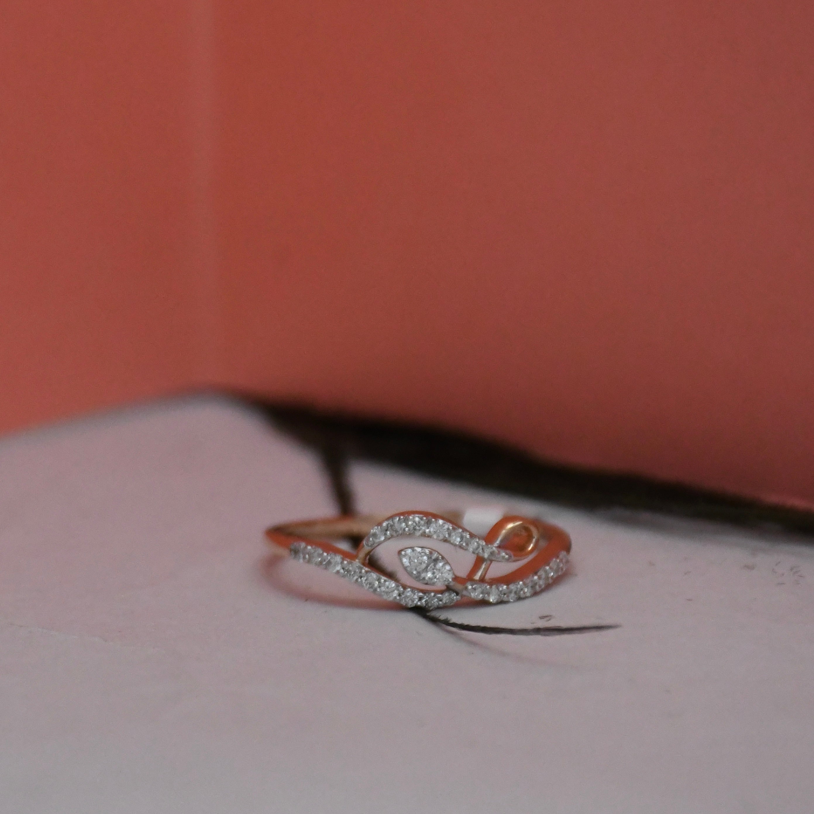 A rose gold ring with a gold pavé band and a central clear diamonds, resting on a white surface with a coral orange background.