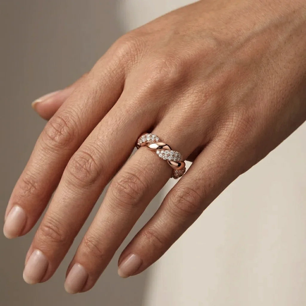 Hand wearing a rose gold ring with diamonds on a neutral background