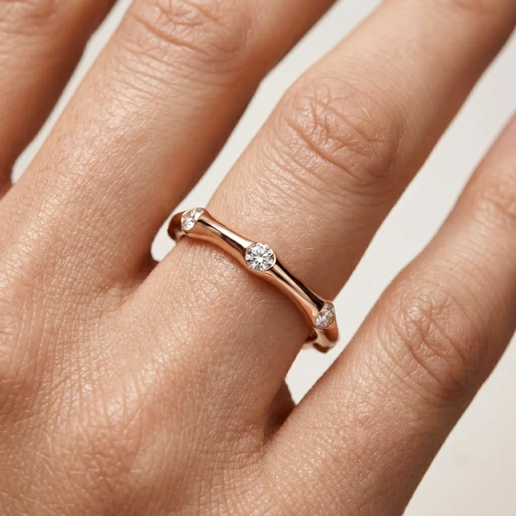 Rose gold ring with diamonds on a hand against a neutral background