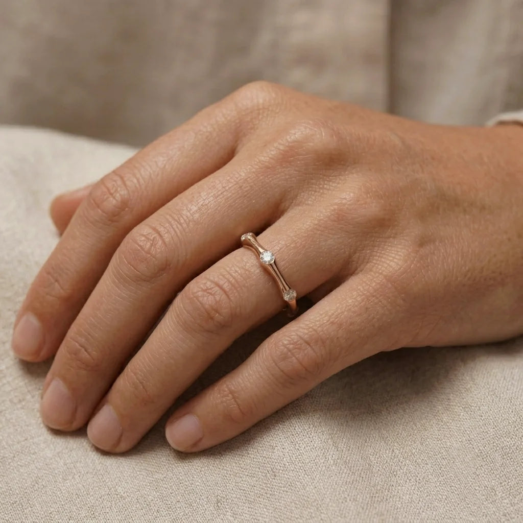 Hand wearing a rose gold ring with diamonds on a beige fabric background