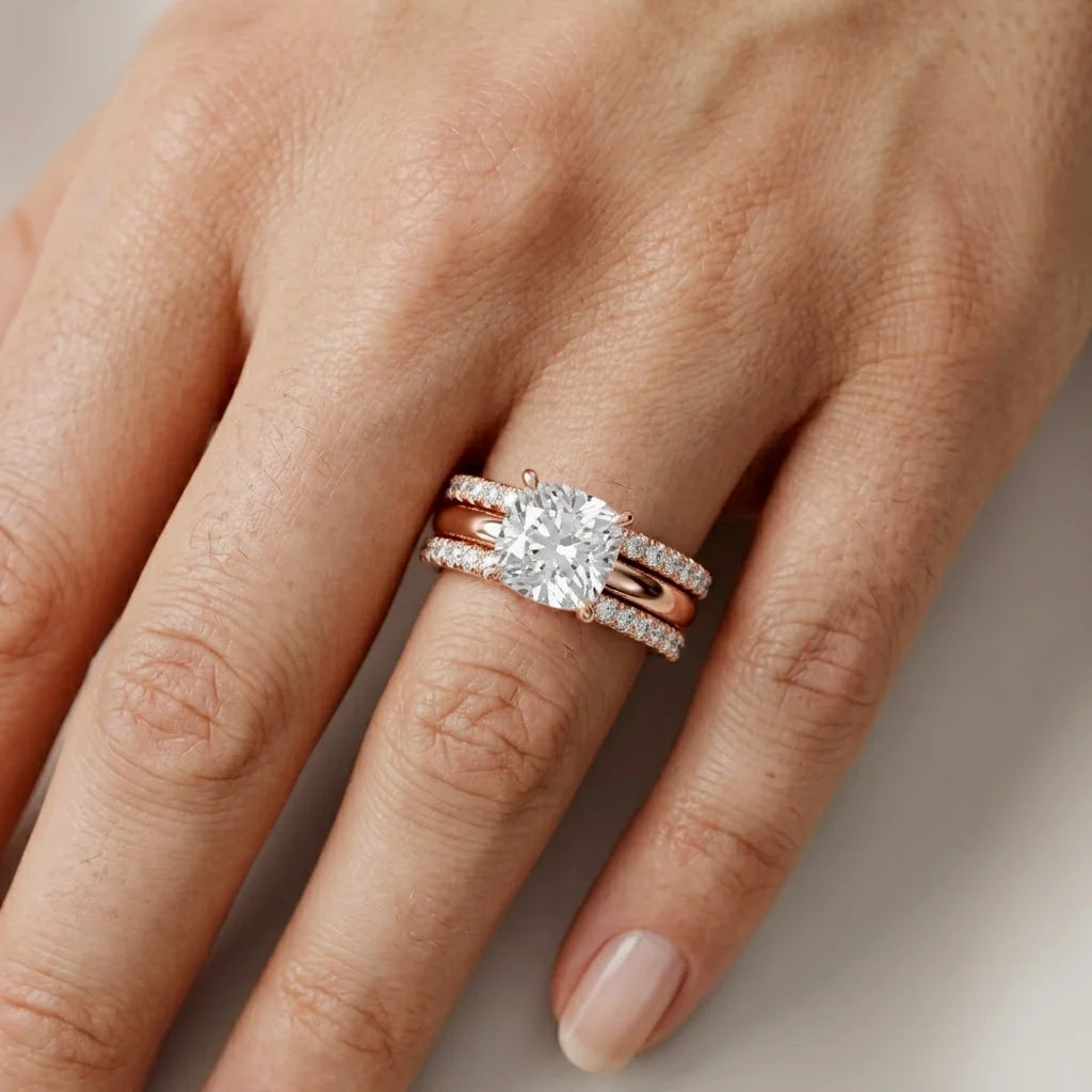 Rose gold ring with a large diamond and small diamonds on a hand against a neutral background