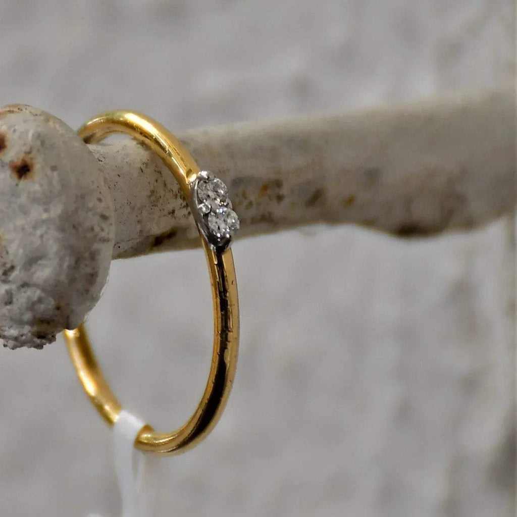 A gold band ring with two diamonds set on top, positioned on hanger.