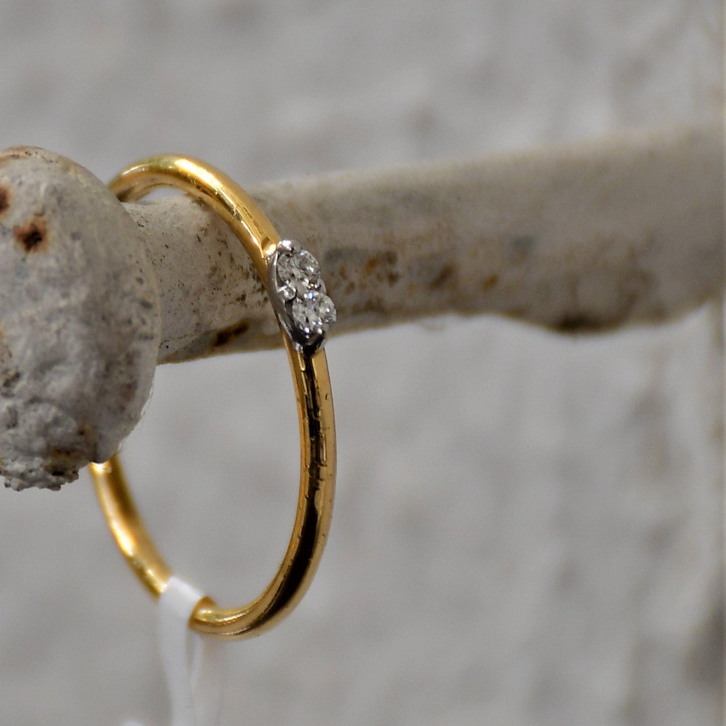 A gold band ring with two diamonds set on top, positioned on hanger.