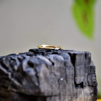 A gold band ring with two diamonds set on top, positioned on dark rough stone surface.