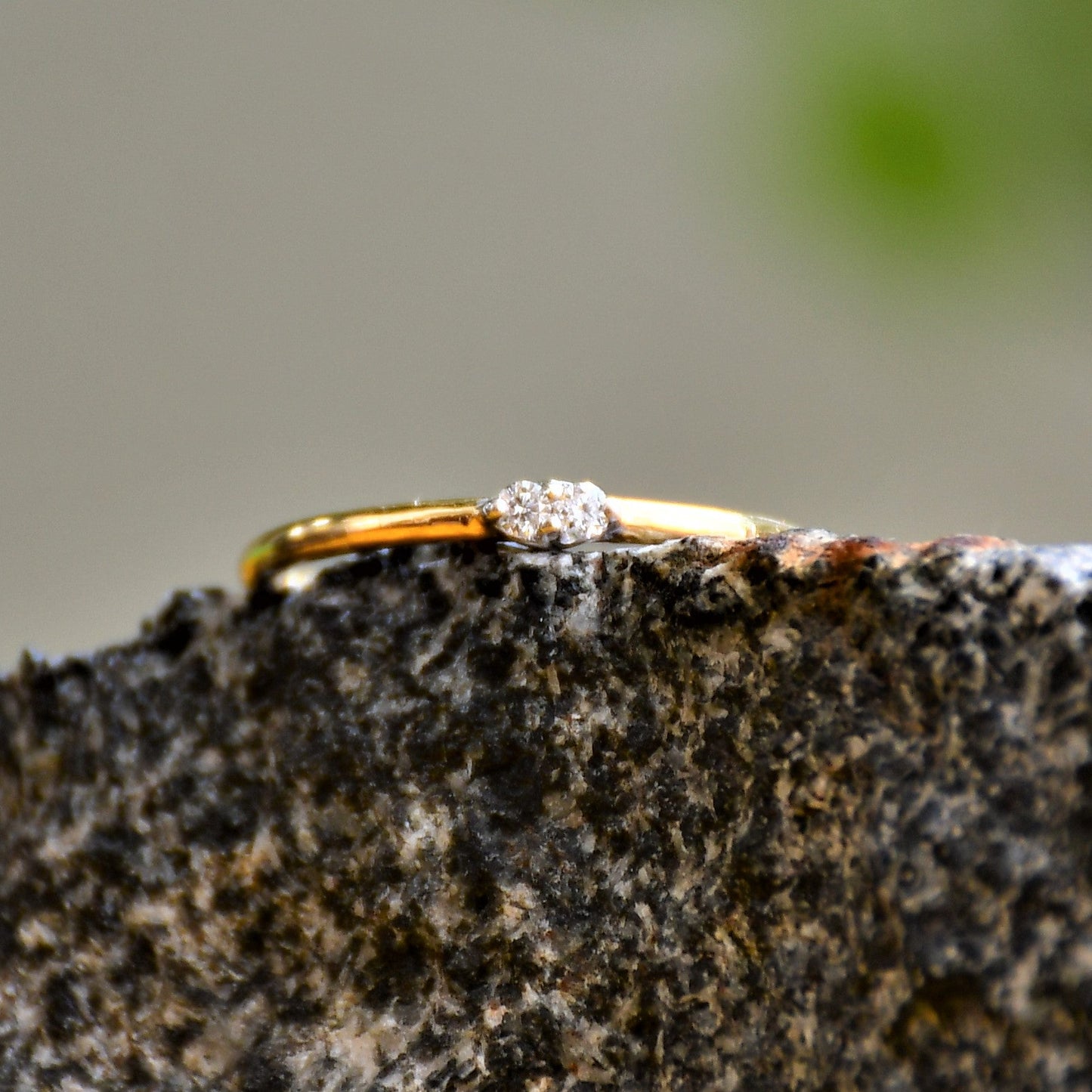 A gold band ring with two diamonds set on top, positioned on a textured dark stone surface.